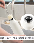 Person cleaning a bambaw wide mouth insulated bottle with a brush in a kitchen setting, emphasizing the wide mouth design.