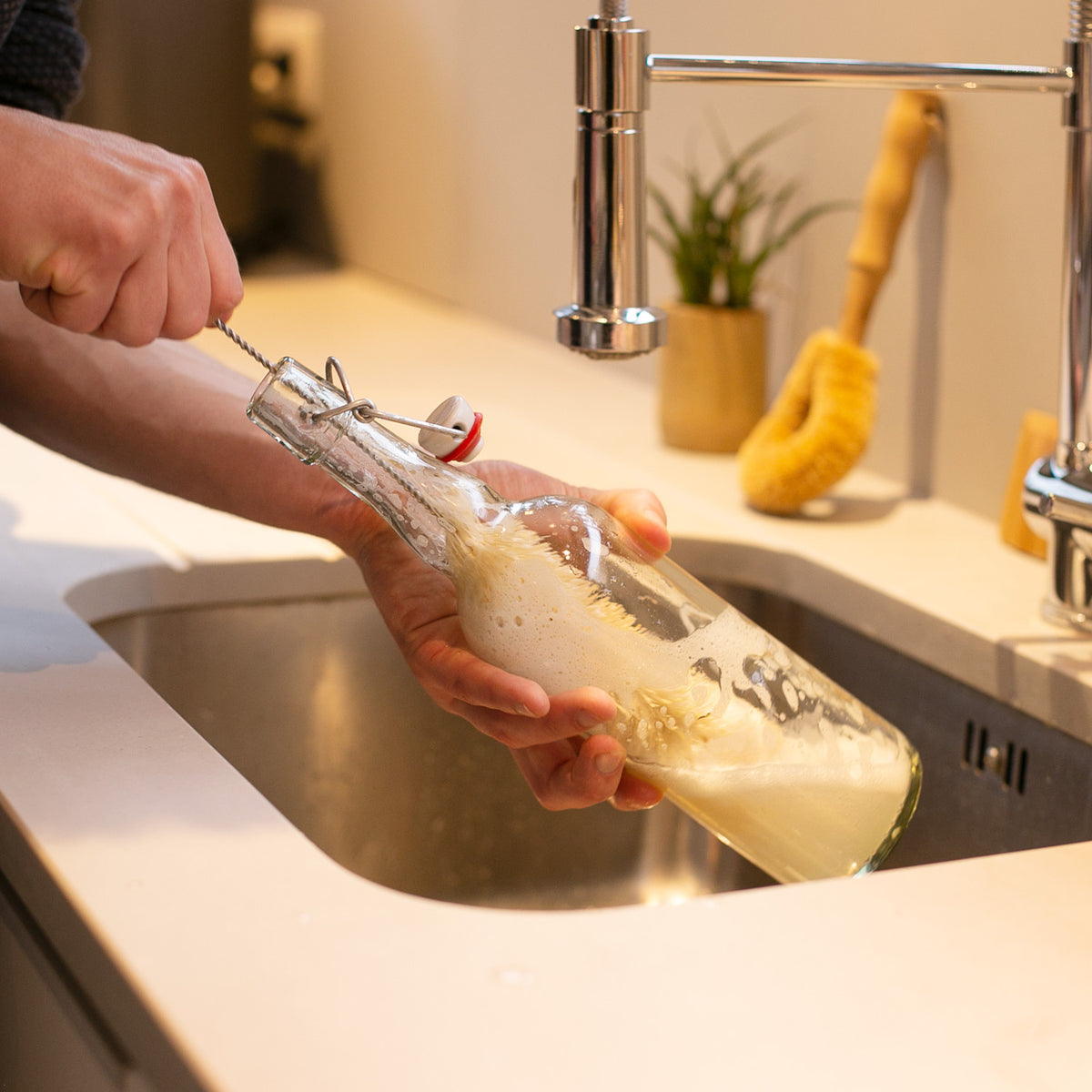 A person washing a glass bottle with a bambaw plastic-free bottle cleaning brush