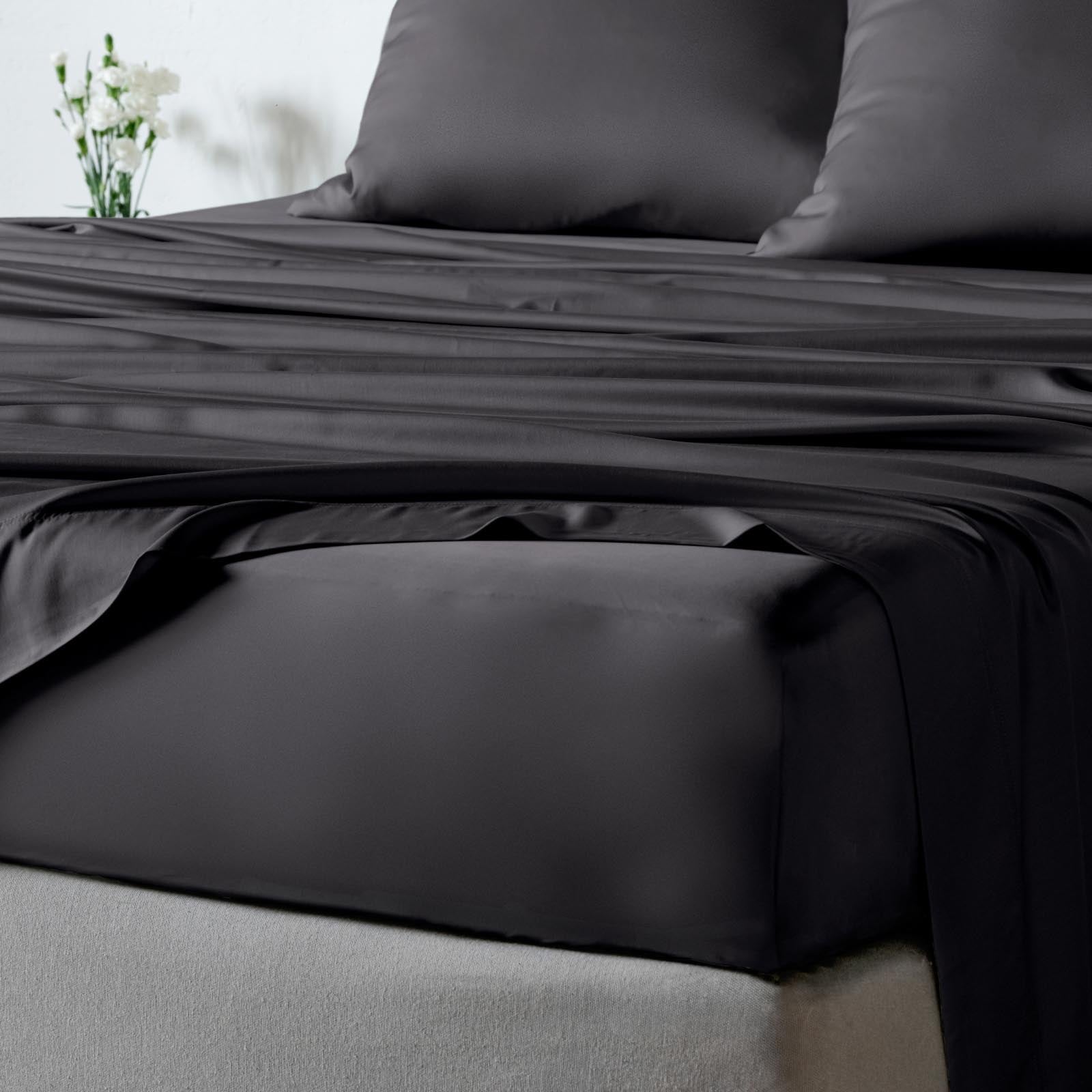 Black bambaw cozy bamboo bed sheet set with a fitted sheet and matching pillowcases on a bed, with a small vase of white flowers in the background.