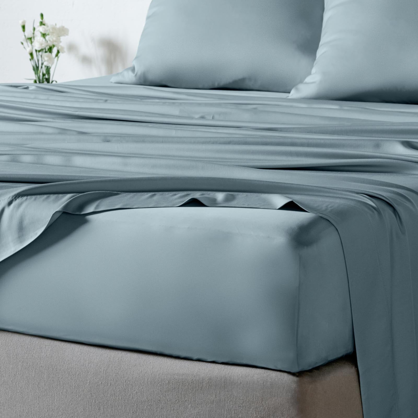 A close-up of bambaw cozy dusty blue fitted bed sheet dressed in a smooth, sheet set with matching pillowcases and a fitted sheet draped over the corner.